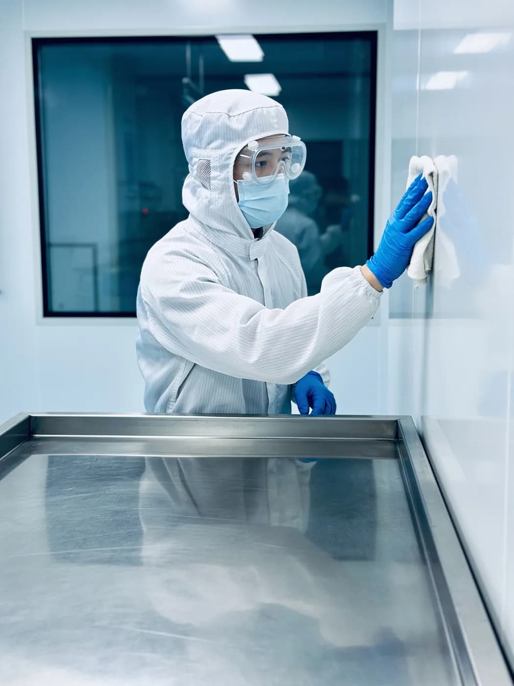 Cleanroom operative in a protective suit wiping a stainless steel surface in pharmaceutical manufacturing